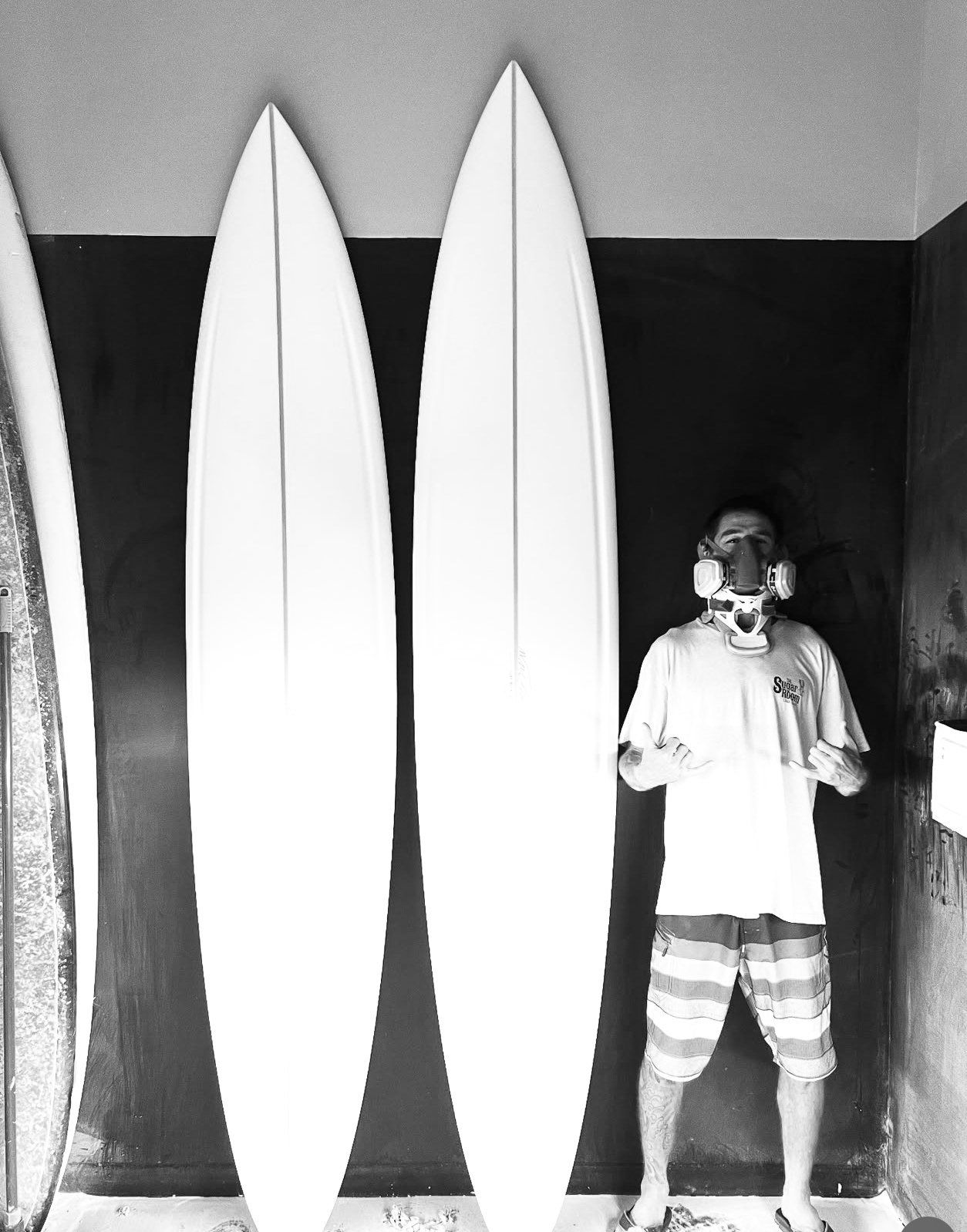 Will Scovel in his shaping bay wearing a respirator, standing beside two boards